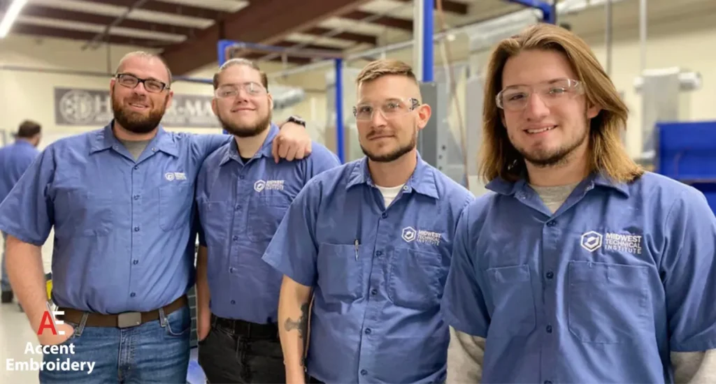 Four men in blue shirts stand together inside a factory, engaged in a discussion about their work. Four men in blue shirts stand together inside a factory, engaged in a discussion about their work.