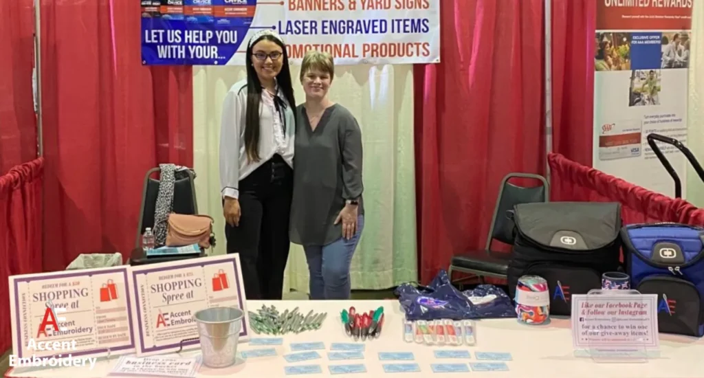 Two women are positioned by a table highlighting laser engraving options at Accent embroidery